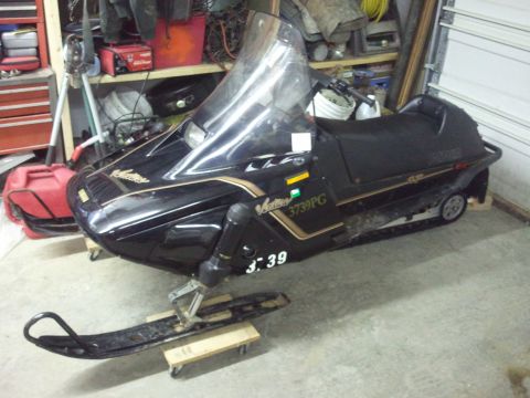 1985 Ford Bronco - A black snowmobile with gold accents is parked indoors on a concrete floor.