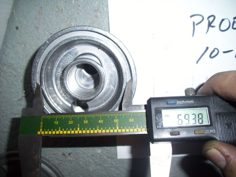 Oil filter housing being measured with digital calipers showing 69.38mm. Text on housing reads 'MADE IN USA'