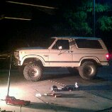 1986 Ford Bronco - Side view of a tan 1980s Ford Bronco, parked with repair equipment nearby.
