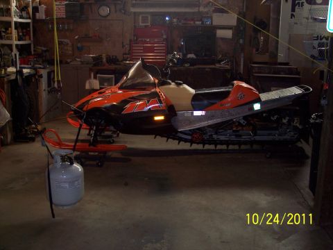 2004 Arctic Cat King Cat 900 - An orange and black snowmobile is parked inside a garage, with a propane tank in the foreground.