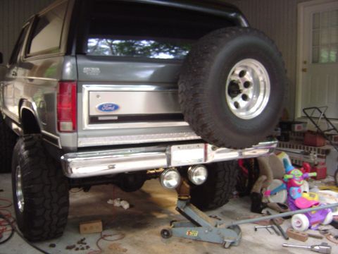 1986 Ford Bronco - Rear view of a lifted 1986 Ford Bronco, a spare tire, chrome bumper, and dual exhaust pipes.