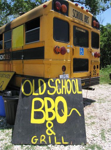 1990 Ford Bronco - A yellow school bus is parked outdoors, with a hand-painted sign in front advertising 'Old School BBQ & Grill'.