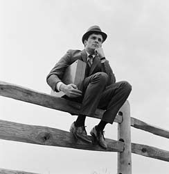 1990 Ford Bronco - Man in a suit and hat sits on a wooden fence, holding a briefcase.