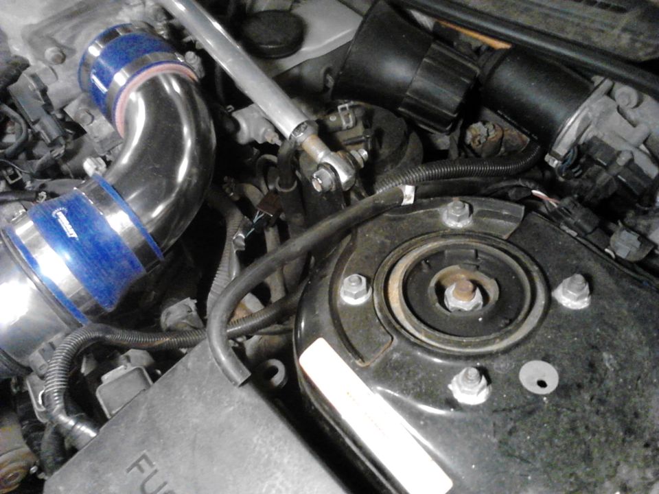 Engine bay with aftermarket intake tube, strut tower, and fuse box. Visible text 'SUPERMOTORS.NET'