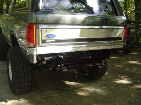 1986 Ford Bronco - Rear view of a lifted silver Ford Bronco, showing the bumper area and chrome trim with a Ford logo.