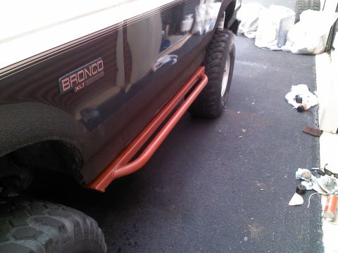 1979 Ford Bronco - Side view of a dark blue Ford Bronco XLT with orange side steps and large tires.