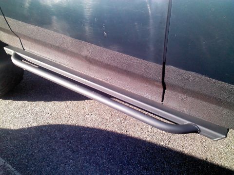 1979 Ford Bronco - Close-up view of aftermarket side step bars mounted to a dark-colored vehicle.