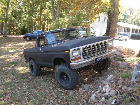 1978 Ford Bronco - A black 1978 Ford Bronco is shown with a lifted suspension and large tires, parked on uneven terrain.