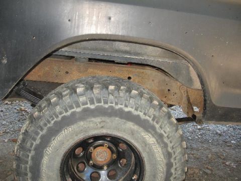 1978 Ford Bronco - This image shows a close-up of a vehicle's wheel well, revealing a large tire and rusty suspension parts, suggesting off-road modifications.
