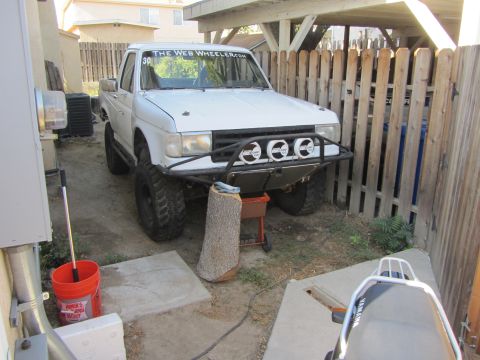 1968 Ford Mustang - A modified white pickup truck is parked in a yard next to a wooden fence and some trash cans.