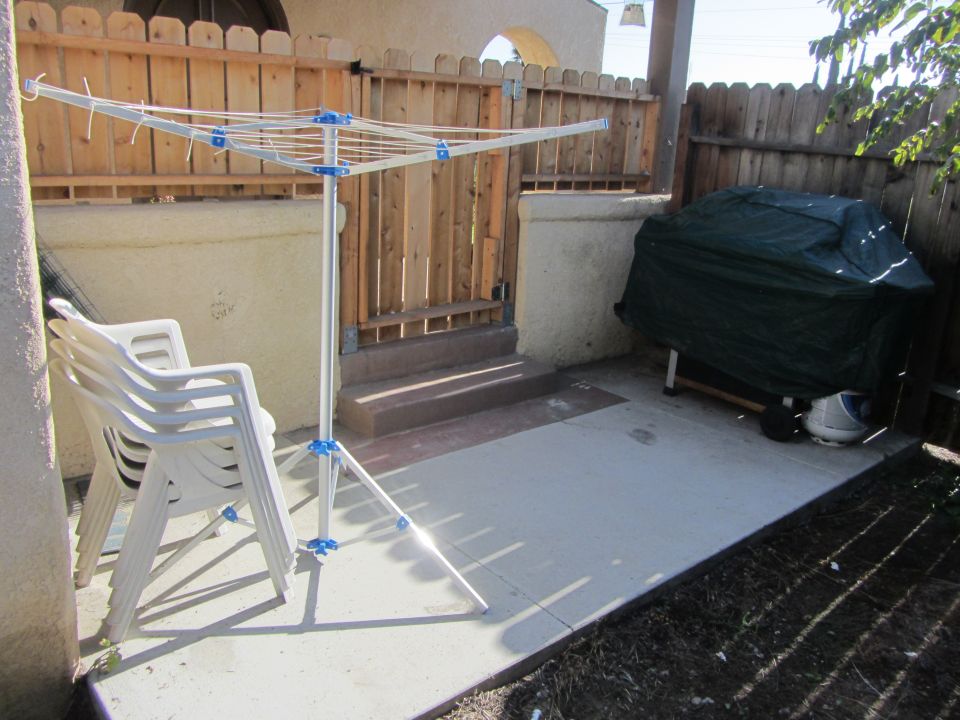 Patio scene with a folding clothesline, stacked chairs, and a covered grill