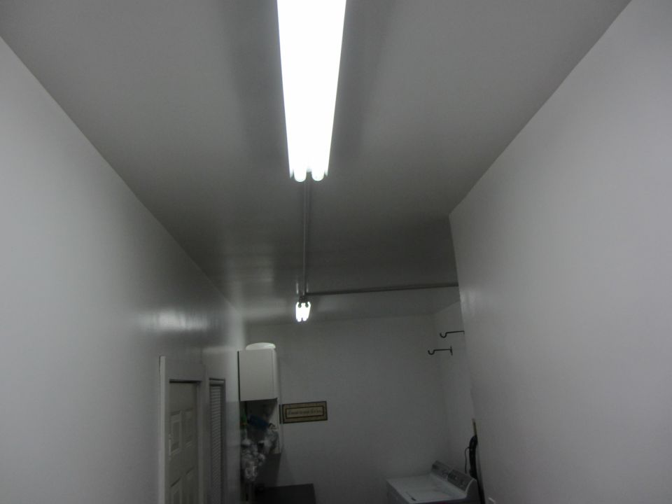 Interior scene with fluorescent lights, white walls, a door, and a washing machine