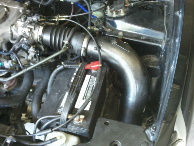 Engine bay showing a car battery and custom intake piping