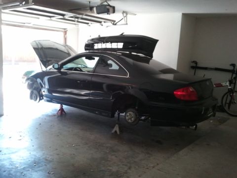 2008 Subaru Legacy - A black coupe is raised on jack stands in a garage, with its hood and trunk open and a roof box mounted on top.