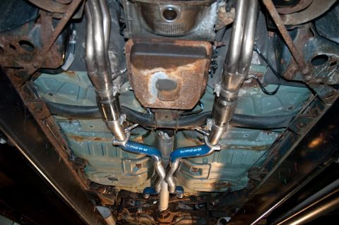 1998 Ford Crown Victoria - The underside of a 1998 Ford Crown Victoria reveals a dual exhaust system with blue hangers and visible rust on the frame.