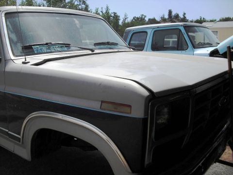 1986 Ford Bronco - Two trucks are parked side-by-side, showing their front ends and hoods.