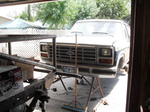 1986 Ford Bronco - A 1986 Ford Bronco is seen from the front, elevated on jack stands in a garage setting.