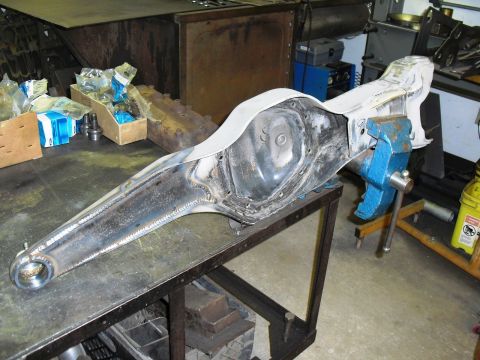1986 Ford Bronco - A rear axle assembly is secured in a blue vise on a workbench, surrounded by tools and parts.