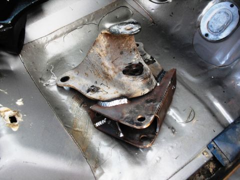 1986 Ford Bronco - Close-up of a rusted suspension bracket welded onto a metal floor, likely part of a vehicle's undercarriage.