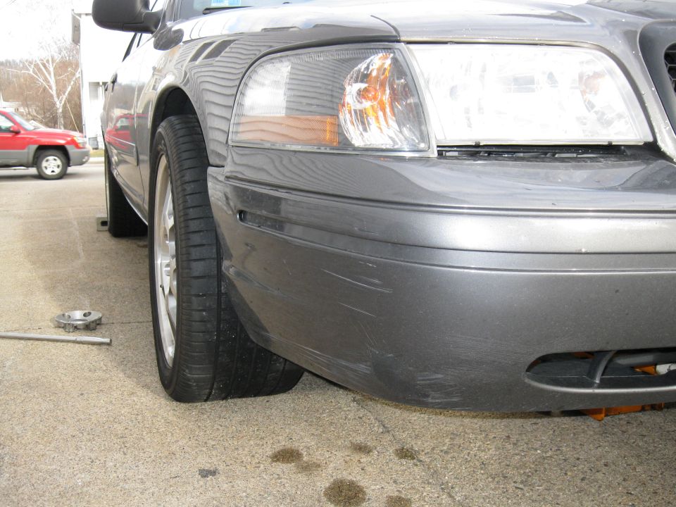 Gray Ford Crown Victoria with a flat tire, front passenger side visible, showing scratches on bumper