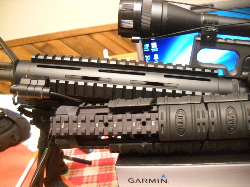 Close-up of an assault rifle with a scope mounted on top, showing picatinny rails and accessory mounts