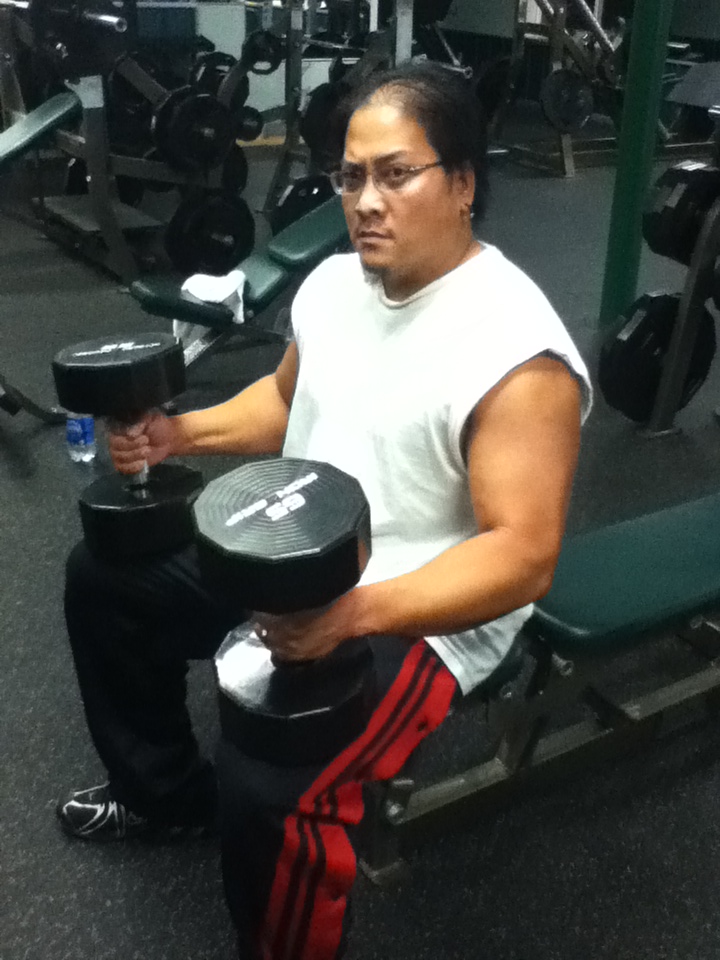 Man with glasses and white t-shirt lifting dumbbells in a gym