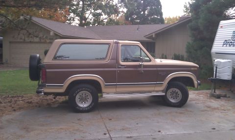 1984 Ford Bronco - Side view of a two-tone Ford Bronco with a spare tire mounted on the back.