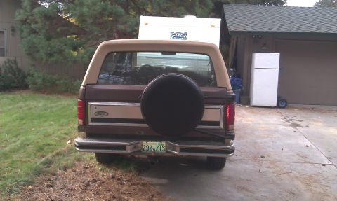 1984 Ford Bronco - Rear view of a brown Ford Bronco with a tan top and a spare tire mounted on the back.