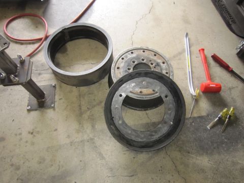 1996 Ford Bronco - Various brake drum components and tools, including a rubber seal, metal drum, and a mallet, are laid out on a concrete surface.