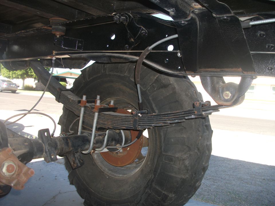 Underside of a vehicle showing the rear axle, large tire, and leaf spring suspension system