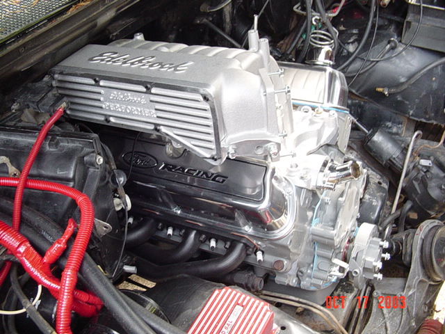 Installed V8 with Edelbrock intake and Ford Racing valve covers, red plug wires, in an engine bay