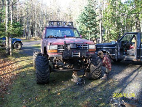 1988 Ford F-250 - Two trucks are parked outside with one being worked on. The truck on the left has very large tires.