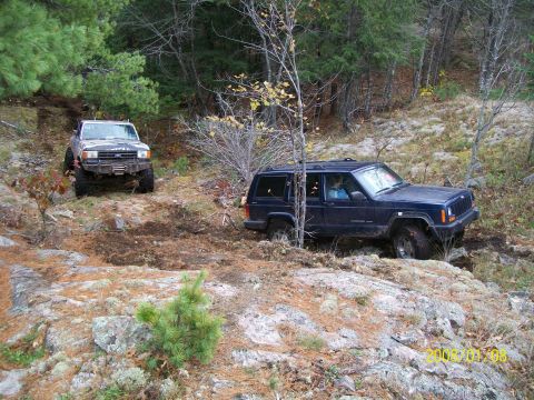 1988 Ford F-250 - A dark blue Jeep Cherokee XJ navigates a rocky trail with another vehicle in the background.