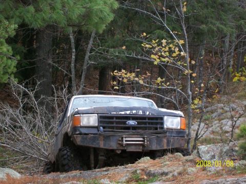 1988 Ford F-250 - A Ford truck is parked on a rocky, wooded area with a winch mounted on the front bumper.