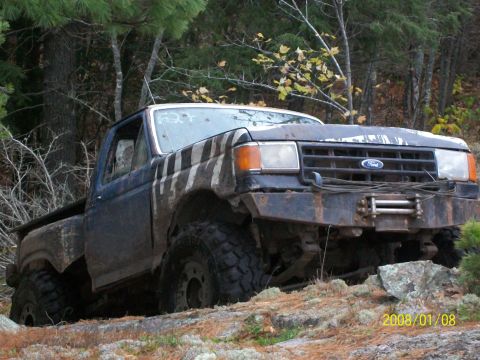 1988 Ford F-250 - A modified Ford F-250 navigates a challenging, wooded, rocky landscape.