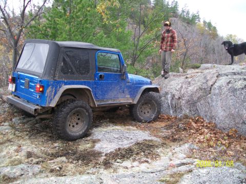 1988 Ford F-250 - A blue Jeep Wrangler navigates a rocky trail with a person and a dog observing.