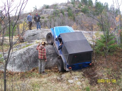1988 Ford F-250 - A blue off-road vehicle navigates a rocky terrain with onlookers observing the challenging maneuver.