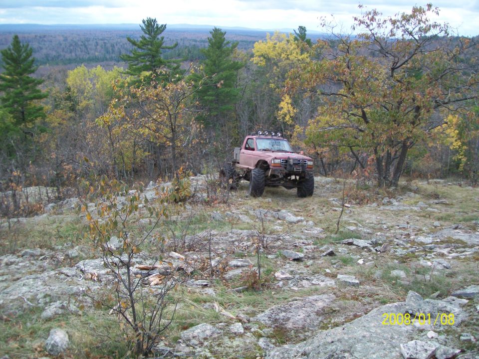 Red pickup truck with large tires and off-road lights on rocky terrain