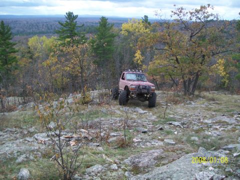 1988 Ford F-250 - Modified 1988 Ford F-250 navigating a rocky, wooded landscape during autumn.