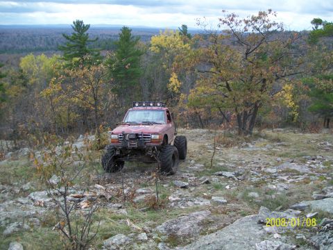 1988 Ford F-250 - A modified pickup truck navigates a rocky, wooded landscape during autumn.