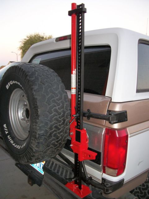 1996 Ford Bronco - Rear view of a white and tan Ford Bronco with a spare tire and a red Hi-Lift jack attached.