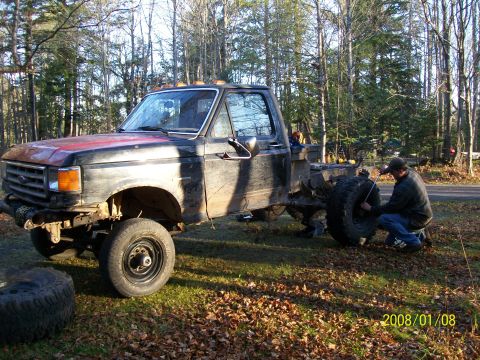 1988 Ford F-250 - A man works on a tire of a black and red pickup truck in a wooded area.