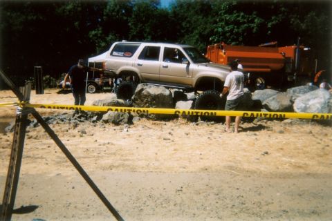 1988 Ford Bronco - This modified SUV is navigating a rocky obstacle course, with a dump truck visible in the background.