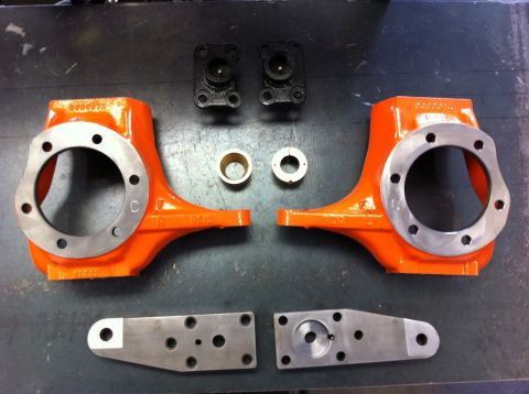 Suzuki Samurai - Various metal parts, including orange axle knuckles and mounting plates, are laid out on a dark surface.