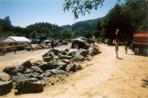 1988 Ford Bronco - A pickup truck attempts an obstacle course in a rocky outdoor arena with spectators present.