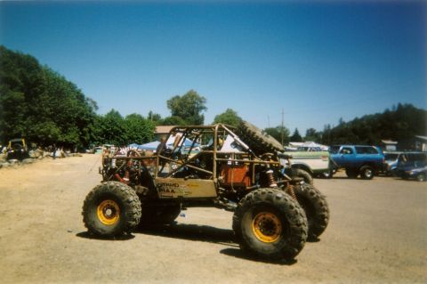 1988 Ford Bronco - A heavily modified off-road buggy with a prominent roll cage and large tires is parked outdoors, with other vehicles visible in the backgro…