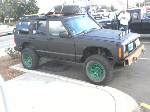 1998 Jeep Cherokee - A modified 1998 Jeep Cherokee is parked on a curb, equipped with off-road accessories.