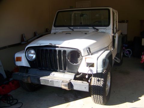 2000 Jeep TJ - A white Jeep Wrangler is shown from the front, parked in a garage with its grille and one headlight visible.
