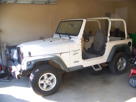 2000 Jeep TJ - This white 2000 Jeep TJ Wrangler 4.0L Sport is seen in a garage, its iconic roll cage and 'Sport' badging.