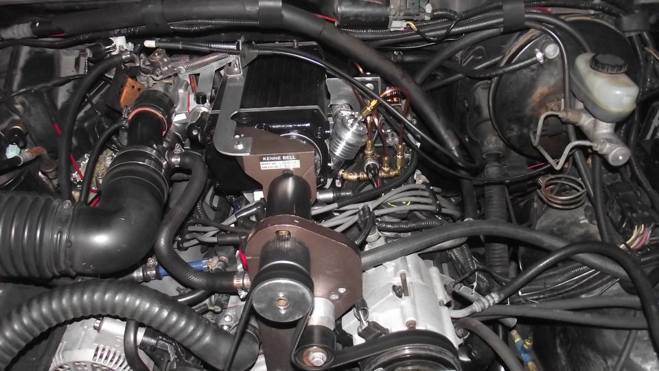 Engine bay with Kenne Bell supercharger, ribbed intake hose, and bronze pulley bracket on a V8
